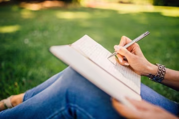 Ragazza che scrive su un quaderno, seduta in un prato.